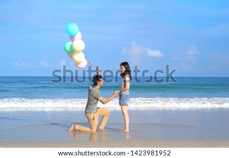 Happy Asian couple holding colorful balloons at the beach during travel trip on holidays vacation outdoors at ocean or nature sea at noon, Phuket, Thailand