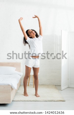 cheerful african american woman stretching, standing in white bright room at home