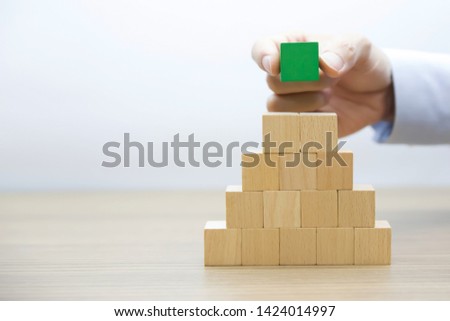 On The Right hand side Fourteen Wooden cube and one Green Block Stacked on top in Pyramid shape without graphics for Business and design concept, Symbol of leadership, Teamwork and Growth.