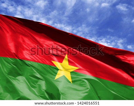 waving flag of Burkina Faso close up against blue sky