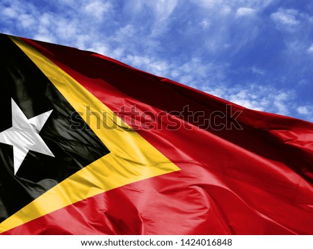 waving flag of East Timor close up against blue sky
