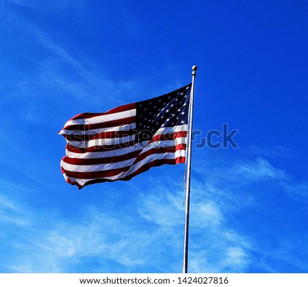 American flag, high in the sky, blowing in the wind, on a clear, sunny day.  Blue sky.  White clouds.  National symbol.  American pride.