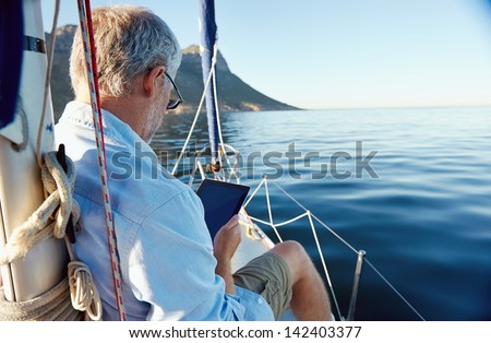 sailing man reading tablet computer on boat with modern technology and carefree retired senior successful lifestyle Royalty-Free Stock Photo #142403377