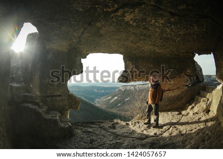 Redhead man in a brown-and-blue windbreaker stands in a cave in the cave city of Mangup-Kale in the Crimea near the city of Bakhchisaray. Travel, adventure, hiking, motivation and speleology concept.