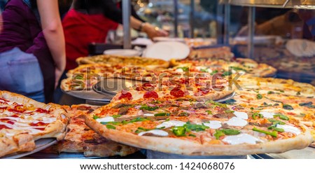 Pizzeria glass window. Variety of italian pizzas in a shop display, street food. Kitchen workers arranging the pizzas. Royalty-Free Stock Photo #1424068076