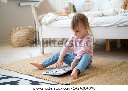 A little two-year-old girl sits on the bedroom floor and plays. Toy calendar in the form of a puzzle. Educational games for children. Bright bedroom, black and white carpet near the bed