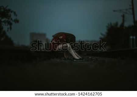 A dramatic picture of a girl walking along a railroad concept of fear of suffering violence and sadness she is stained with her red clothes torn partly visible legs and the rail her head is down