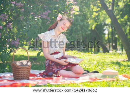 pretty young pin up girl having rest on the nature. happy slim young woman wearing vintage dress sitting on the tartan plaid and relaxing by summer day alone.
