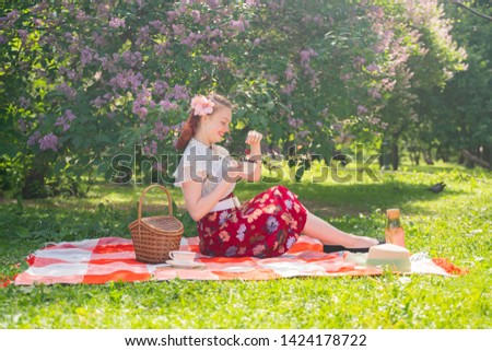pretty young pin up girl having rest on the nature. happy slim young woman wearing vintage dress sitting on the tartan plaid and relaxing by summer day alone.