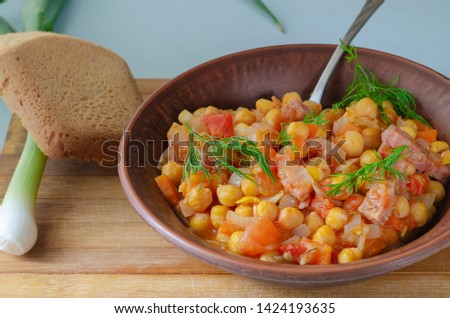 Roasted chickpeas in a clay plate with greens and bread on a wooden board