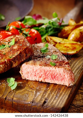 Portion of healthy lean grilled beef steak sliced through to reveal the rare interior served on a wooden board with roast vegetables