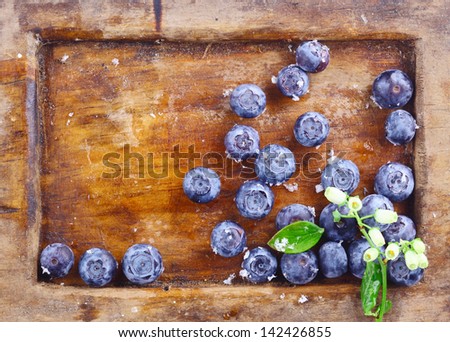 Close-up of a small amount of ripe blueberries or bilberries in an old wooden tray with a small flowery branch