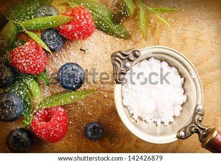 Fresh selection of mixed berries with granulated sugar in a strainer including raspberries and blueberries sprinkled with fine sugar on a wooden background