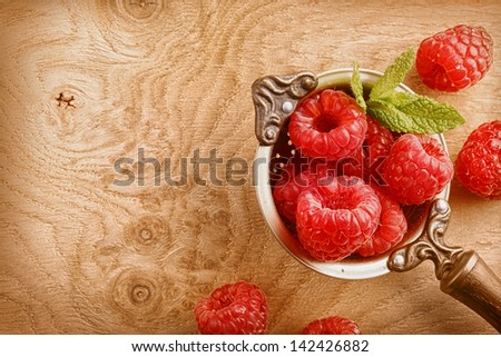 Top view of an old copper ladle filled with ripe raspberries decorated with mint leafs over a wooden table