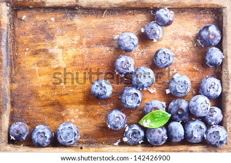 Close-up of a small amount of ripe blueberries or bilberries in an old wooden tray with a green leaf