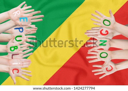 Inscription Republic of the Congo on the children's hands against the background of a waving flag of the Republic of the Congo