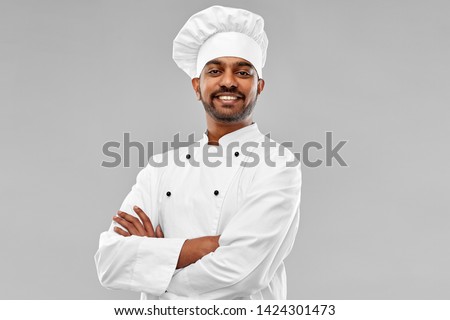 cooking, profession and people concept - happy male indian chef in toque over grey background Royalty-Free Stock Photo #1424301473