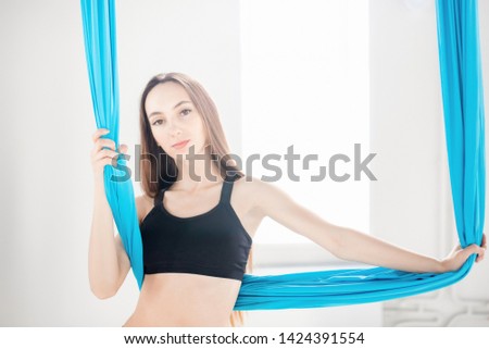 Young beautiful women gymnast in blue hammock. Aerial fly yoga in white studio.