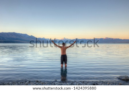 a man standing in water 0 in the background a blue lake and snow-capped mountains