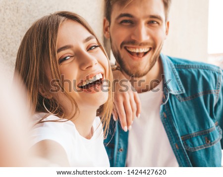 Smiling beautiful girl and her handsome boyfriend in casual summer clothes. Happy family taking selfie self portrait of themselves on smartphone camera. Having fun on the street background  Royalty-Free Stock Photo #1424427620