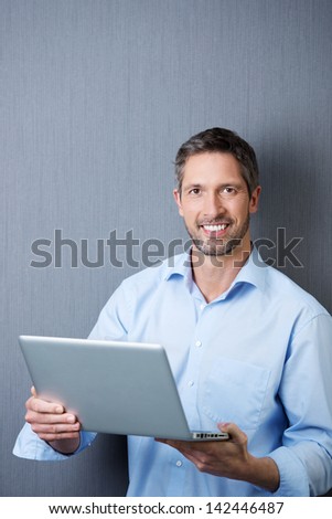 Portrait of confident mature businessman holding laptop against blue wall