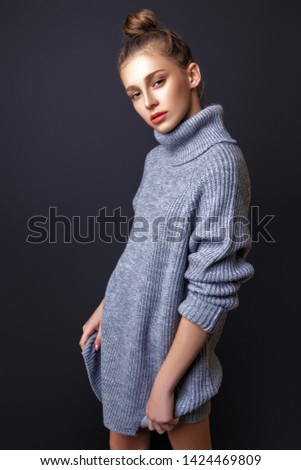 Young beautiful teen girl with collected hair, dressed in a gray free sweater, and posing in the studio on a black background. Fashion concept.