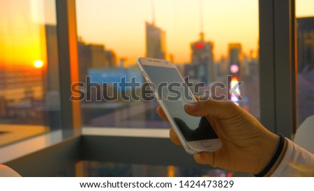 CLOSE UP: Traveler looks at photos while relaxing in her hotel room above Times Square at sunset. Golden evening sunbeams shine on the modern, skyscrapers below unrecognizable woman on her cell phone.