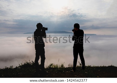 Silhouette of photographer or Traveller using a professional DSLR camera take photo beautiful landscape at the clouds from high up in the hills at Khao Takhian Ngo view point at Khao Kho;Phetchabun