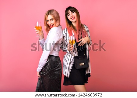 Couple of two pretty funny elegant women drinking champagne end enjoying party time, elegant glamour black and white outfits, trendy pink hairs and background.
