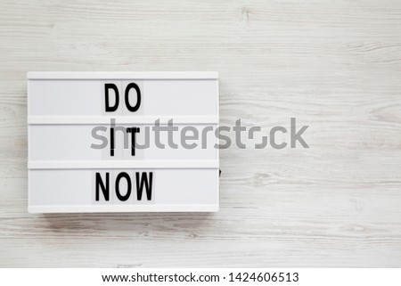 'Do it now' words on a lightbox on a white wooden background. Flat lay, overhead, top view. Copy space.