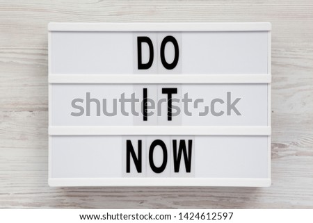 'Do it now' words on a lightbox on a white wooden background, top view. Flat lay, overhead, from above. Close-up.