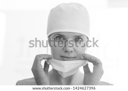 Black and White photo of Closeup portrait of smiling doctor wearing surgical cap removing mask at clinic