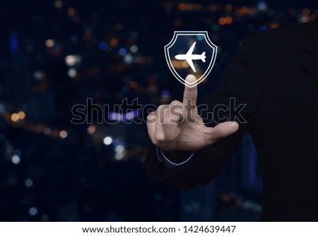 Businessman pressing airplane with shield flat icon over blur colorful night light city tower and skyscraper, Business travel insurance and safety concept