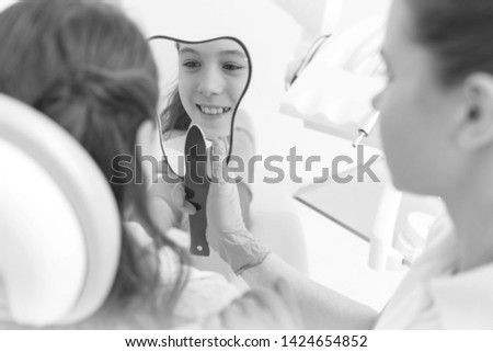 Black and White photo of Dentist showing mirror to smiling girl patient at dental clinic