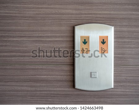 Digital number and down arrow on metallic elevator call panel on wooden pattern wall background with copy space.
