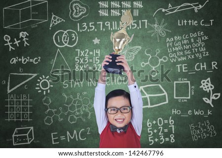 Happy boy raising trophy in classroom