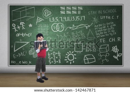 Asian boy reading book with written chalkboard, full length shot