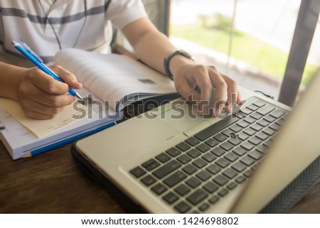 Human hand using laptop and writing note on wooden table