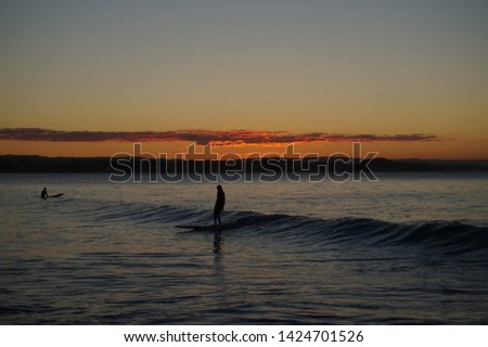 Beginner surfers in the colourful waters of the Pacific ocean as the sun sets over the popular tourist and surf destination of the Gold Coast. Waters are blue and the skies are orange