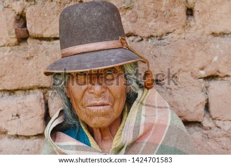 Old native american woman wearing typical aymara clothes. Adobe wall background.