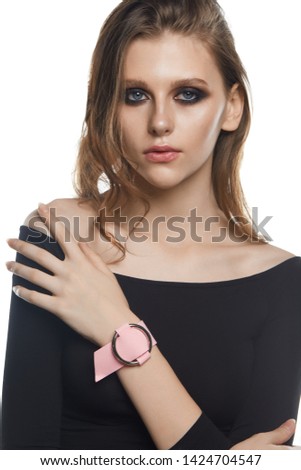 Shot of girl with wavy hair, wearing sweater with cut-away shoulder and pale pink cuff bracelet with silver ring. The woman with smokey eyes is touching and raising her shoulder on white background.