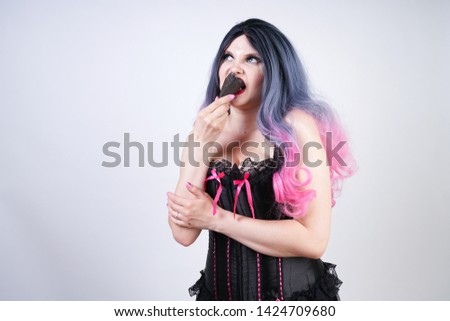 goth girl eating black ice cream in waffle cone. hot plus size woman wearing satin corset with pink bows and enjoys fresh cold tasty sweet ice-cream on white studio background. 