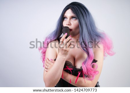 goth girl eating black ice cream in waffle cone. hot plus size woman wearing satin corset with pink bows and enjoys fresh cold tasty sweet ice-cream on white studio background. 