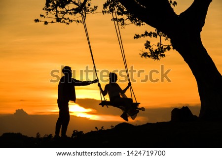 Silhouette couple riding a swing in a beautiful evening sky.