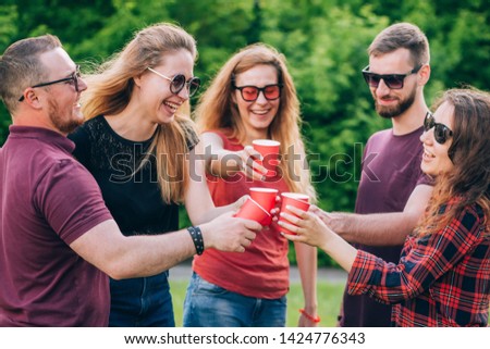 group of happy friends relaxing on nature with red cups of alcohol. celebration, friendship group of smiling friends toasting non alcoholic drinks. red cardboard cup. close-up portrait