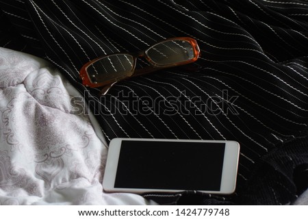 on a black dress with white stripes are glasses and a white smartphone. Lighting - daylight. Concept - morning mess