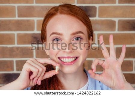 redhaired ginger female with snow-white smile holding white wisdom tooth after surgery removal of a tooth Royalty-Free Stock Photo #1424822162
