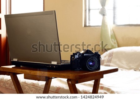 Photo of a laptop computer and a manual, 35mm film camera on a table inside a bedroom