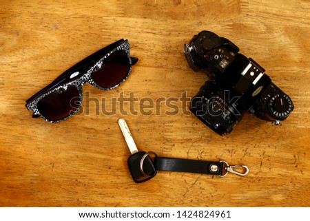 Photo of a manual camera, car key and sunglasses on a table inside a bedroom