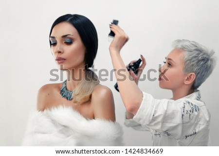Hair stylist straightens hair beautiful model on the set during the break. Hairdresser makes styling a girl before taking pictures
